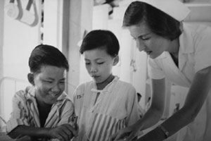 Sadie Stout of Arkansas City, Kansas, who in 1962 was among the first group of Peace Corps volunteers who learned Malay at NIU, works with young patients at Sungei Buloh Leprosarium in Malaysia following her training. (NIU archives)